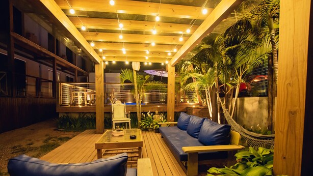 An outdoor patio with wooden flooring, a hammock, and a seating area with cushions. - Pousada Cacau Praia do Rosa (Imbituba)
