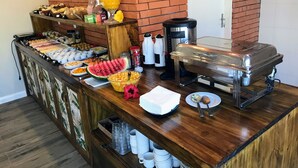 A buffet setup with various food items, a coffee machine, and a fruit bowl. - Pousada Cacau Praia do Rosa (Imbituba)