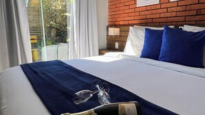 A hotel room with a large bed, a brick wall, and a window with curtains. - Pousada Cacau Praia do Rosa (Imbituba)