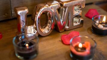 Letras metálicas formando a palavra 'LOVE' sobre uma superfície de madeira, com velas e pétalas de rosa.