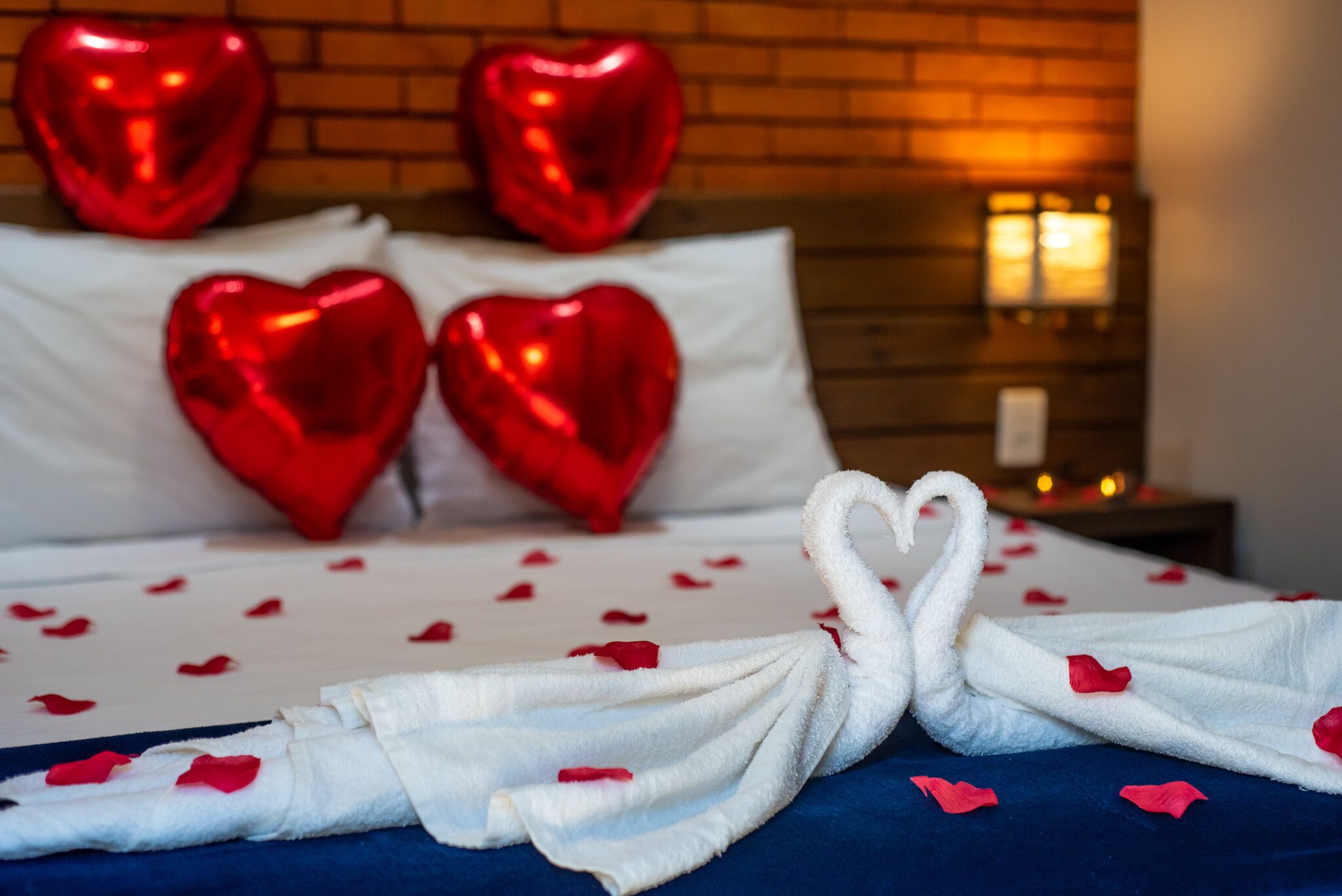 Una cama con almohadones con forma de corazón y una toalla dispuesta en forma de cisne, con pétalos de rosa esparcidos sobre la cama.