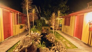 A pathway leading to a building with red doors, surrounded by a garden with rocks and plants. - Pousada Cacau Praia do Rosa (Imbituba)