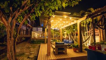 A wooden deck with a hammock, seating area, and potted plants.
