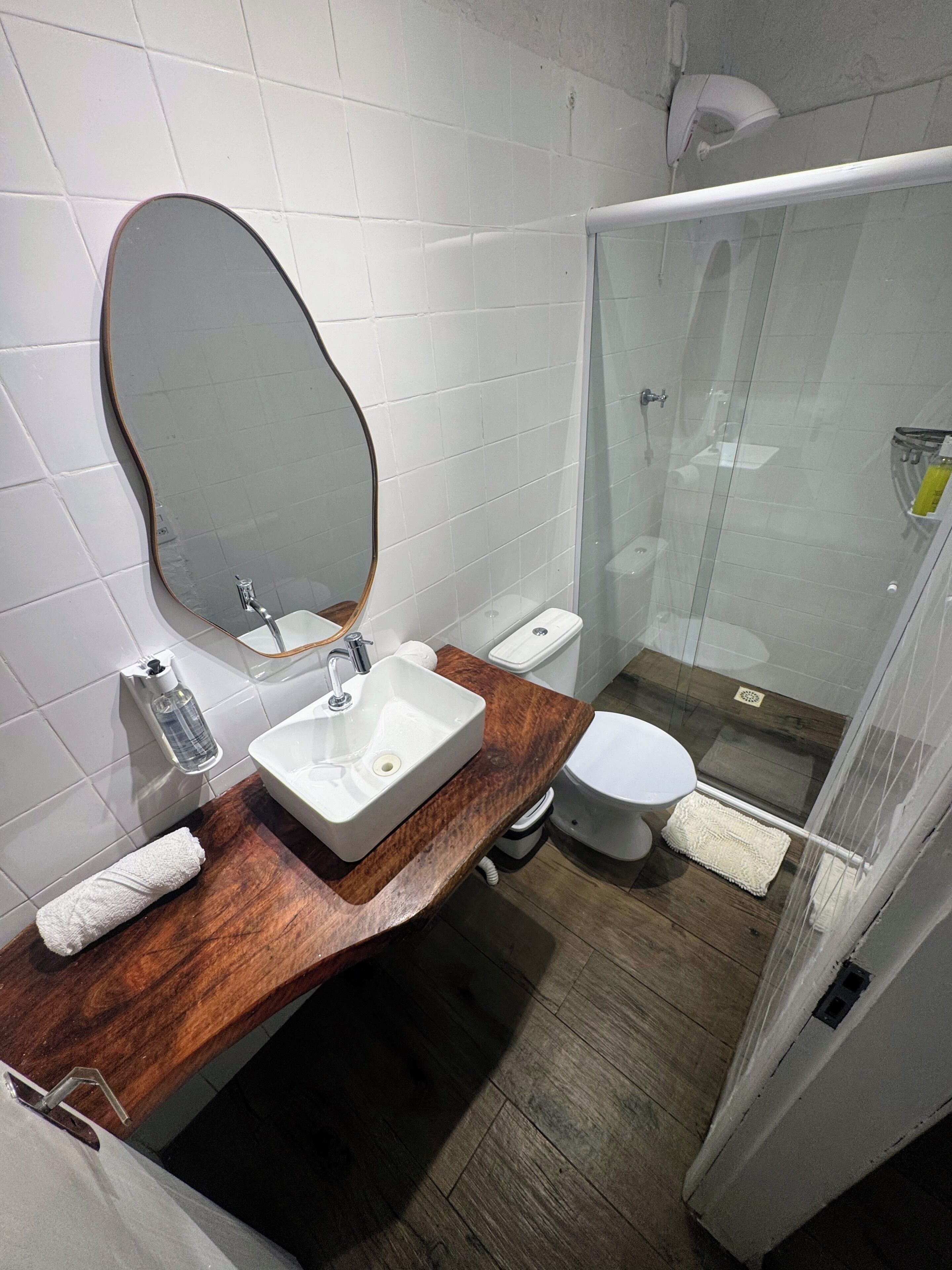 A bathroom with a wooden vanity, a white sink, a mirror, a toilet, and a glass shower enclosure.