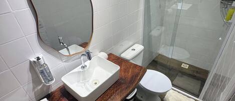 A bathroom with a wooden vanity, a white sink, a mirror, a toilet, and a glass shower enclosure.