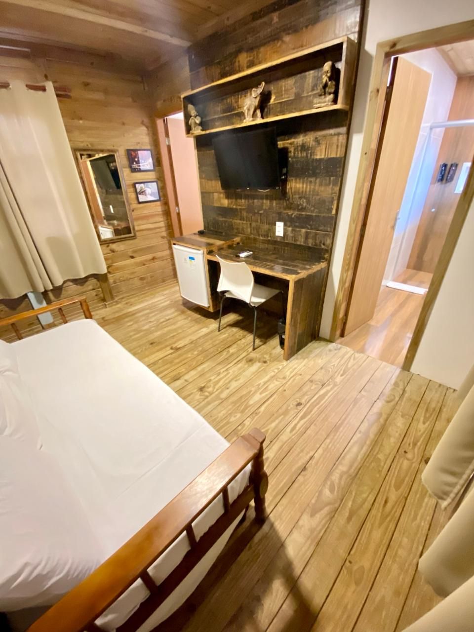 A wooden-floored room with a bed, a desk, and a small refrigerator.