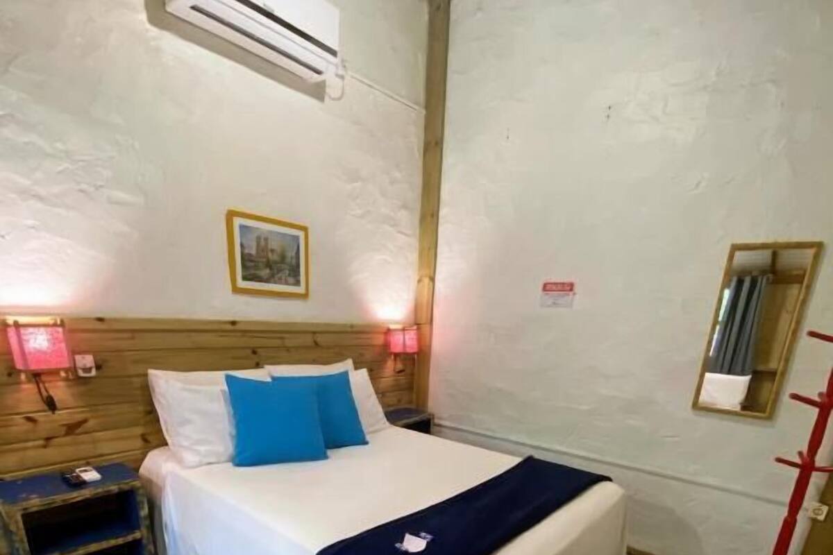A bedroom with a bed, a nightstand, an air conditioning unit, a mirror, and a patterned rug.