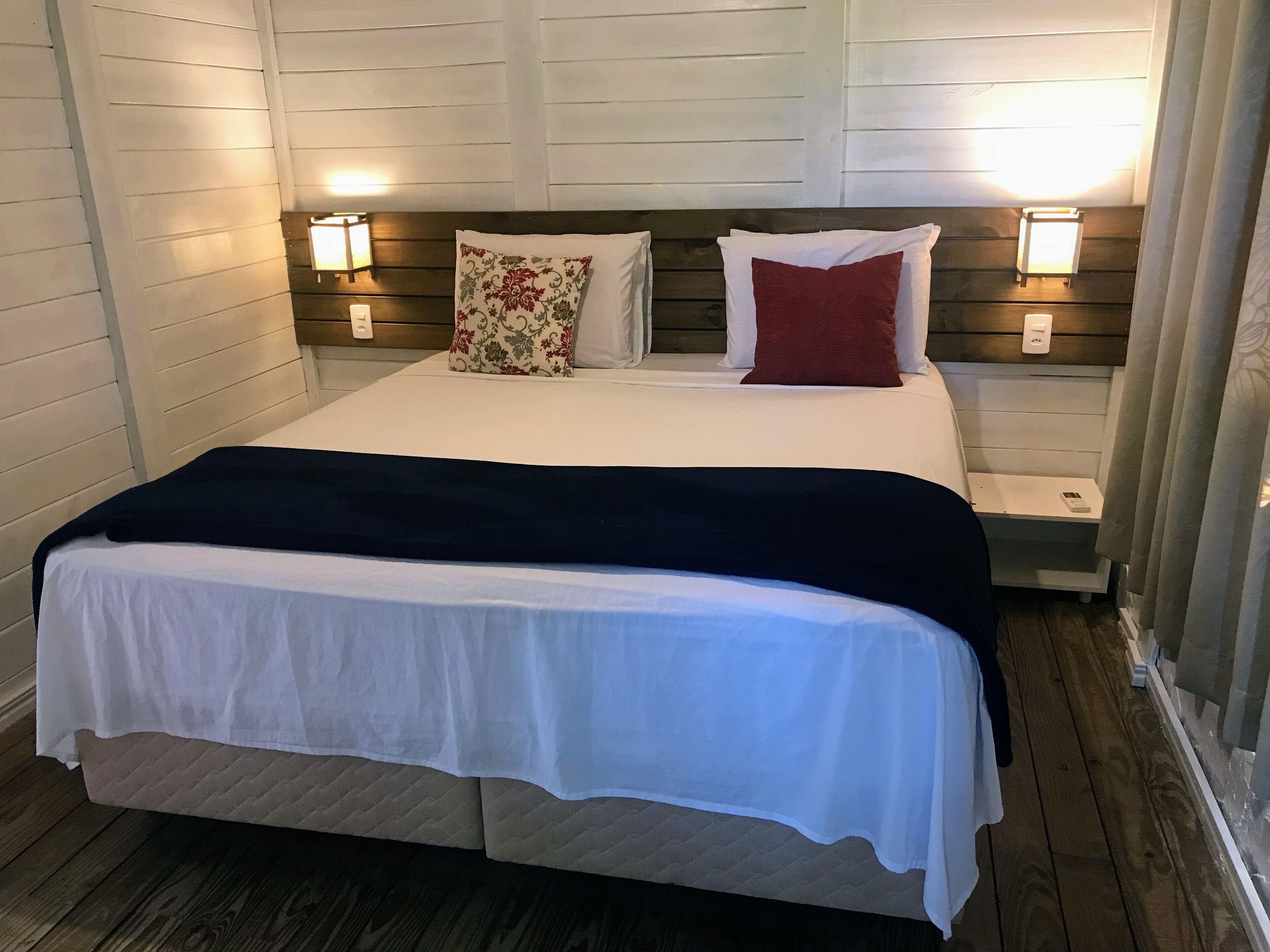 A neatly made bed with a white and navy blue bedspread, two bedside tables with lamps, and a floral pillow.