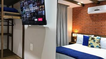 A hotel room with a TV displaying movie posters, a bunk bed, a brick wall, and a bed with blue and white bedding.