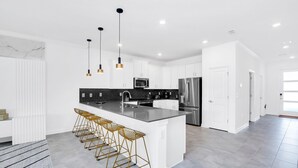 A modern kitchen with white cabinetry, a large island with bar stools, stainless steel appliances, and pendant lighting. - EV_3009 - 9BR / 5BA Storey Lake Villa near to Disney, Private Pool & Games Room (Kissimmee)