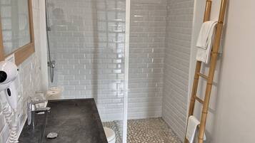 Un baño moderno con ducha envuelta en vidrio, tocador con encimera negra y un taburete de madera.