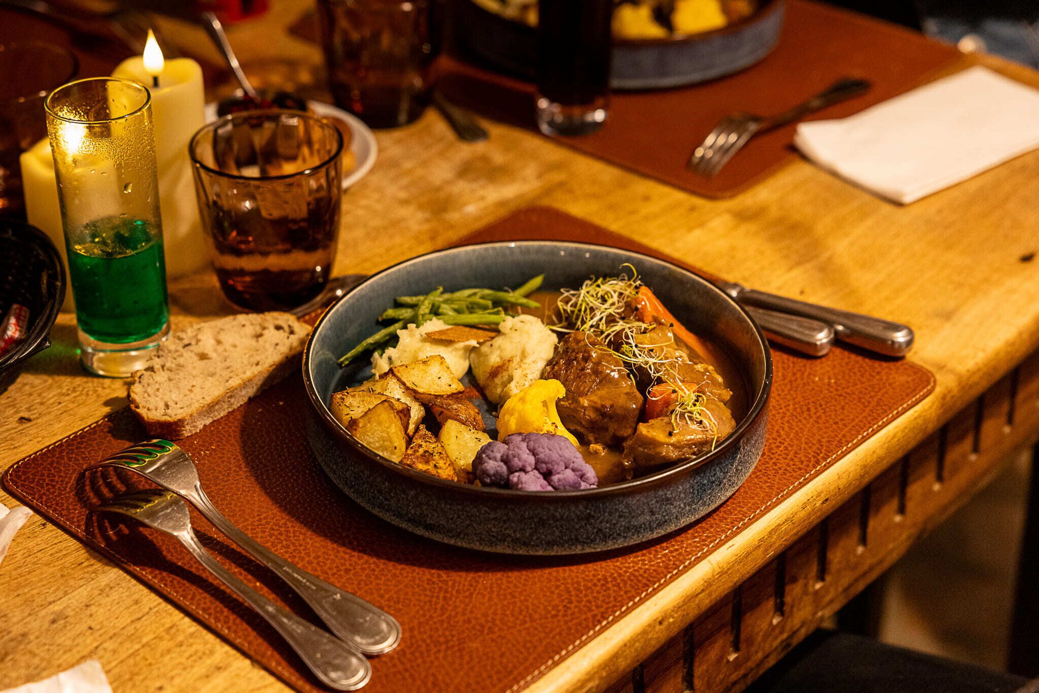A table setting with a plate of food, a glass of green liquid, a candle, and cutlery.