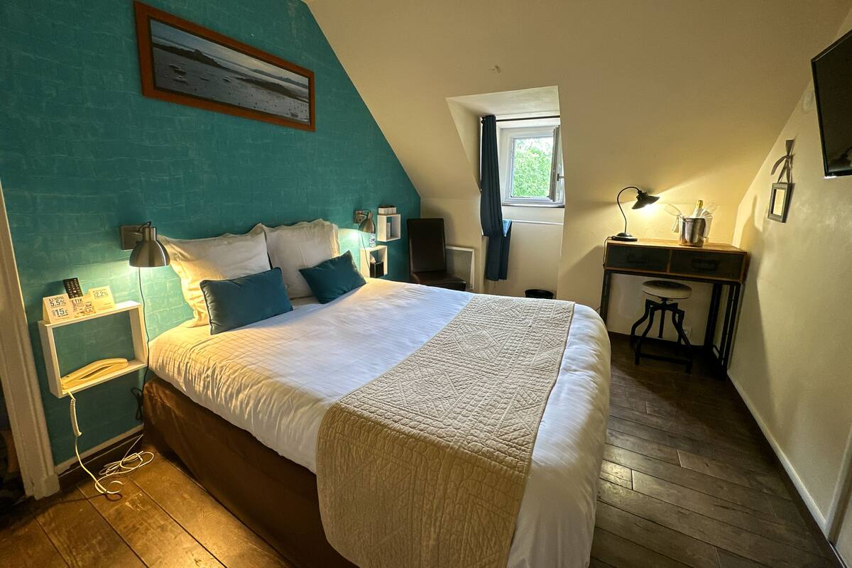 Une chambre à coucher avec un grand lit, un bureau, une chaise, une fenêtre et un téléviseur fixé au mur.