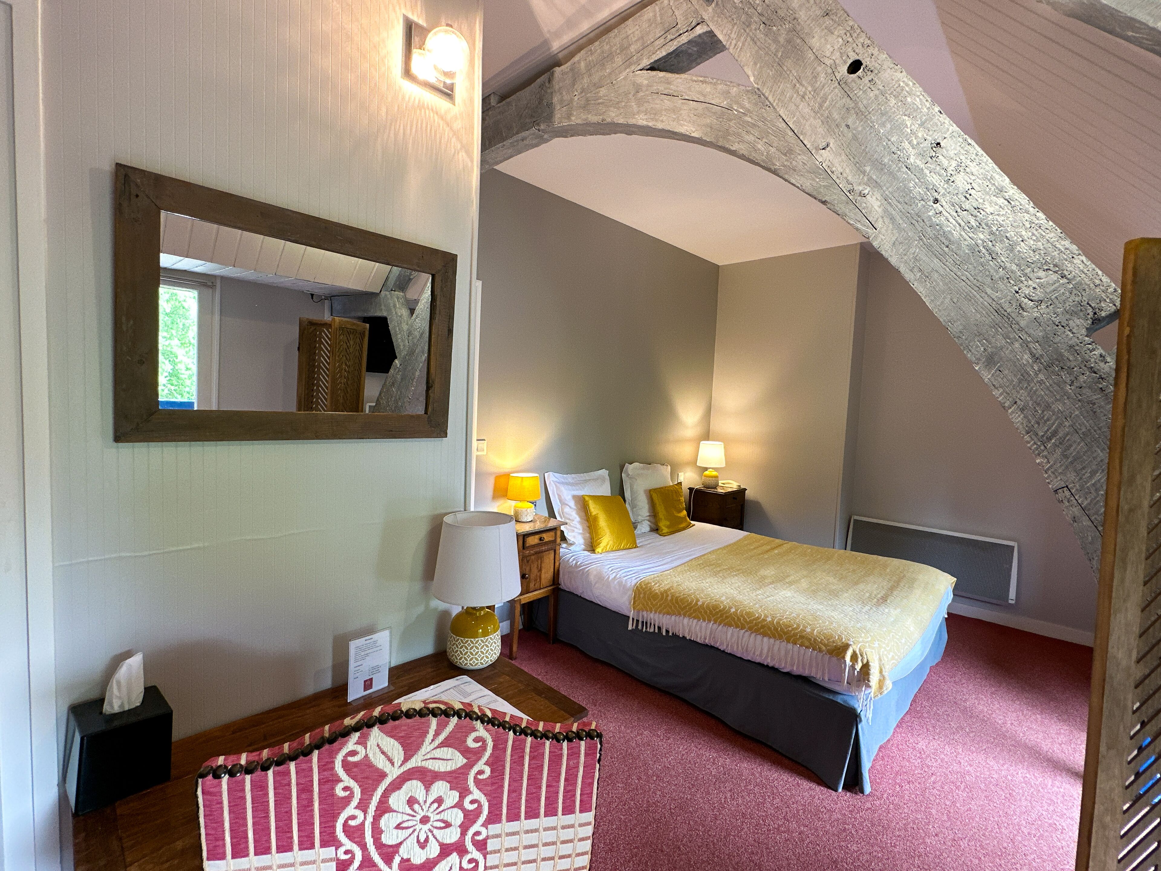 A hotel room with a bed, bedside lamps, a mirror, a bedside table with a lamp, and a decorative cushion.