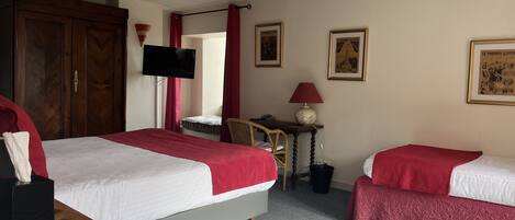 A hotel room with two beds, a wooden wardrobe, a television, a small table with a lamp, and framed pictures on the wall.
