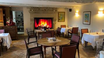 Un espace repas agrémenté d’une cheminée, d’un sol en briques et de tables dressées pour le dîner.