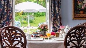 Une table à manger agrémentée d’un arrangement floral, d’un parasol blanc et donnant sur un jardin.