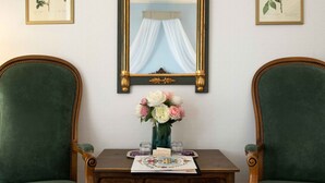 Une pièce comprenant deux fauteuils verts à revêtement en tissu, une table en bois ornée d’un vase de fleurs et un miroir surmonté d’un rideau.