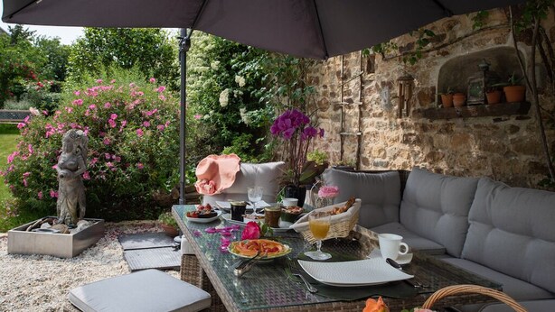 Un espace extérieur aménagé pour prendre les repas, avec une table dressée pour deux personnes, entouré de murs en pierre et de plantes en pot.