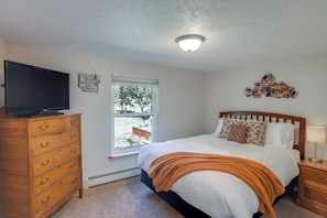 Un dormitorio con cama, cómoda, televisor, ventana y lámpara de techo.