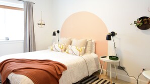A neatly arranged bedroom with a bed, bedside tables, a lamp, and a wall-mounted shelf.