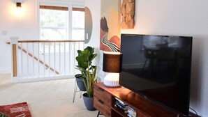 A living room with a large flat-screen TV, a wooden coffee table, a potted plant, and a staircase leading to another level.
