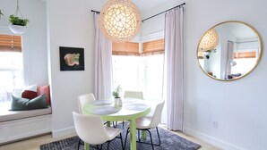 A dining area with a round table, white chairs, a hanging light fixture, and a large mirror on the wall.