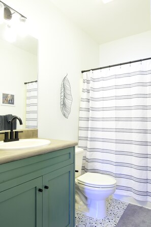 A bathroom with a white sink, a black faucet, a white toilet, and a striped shower curtain.