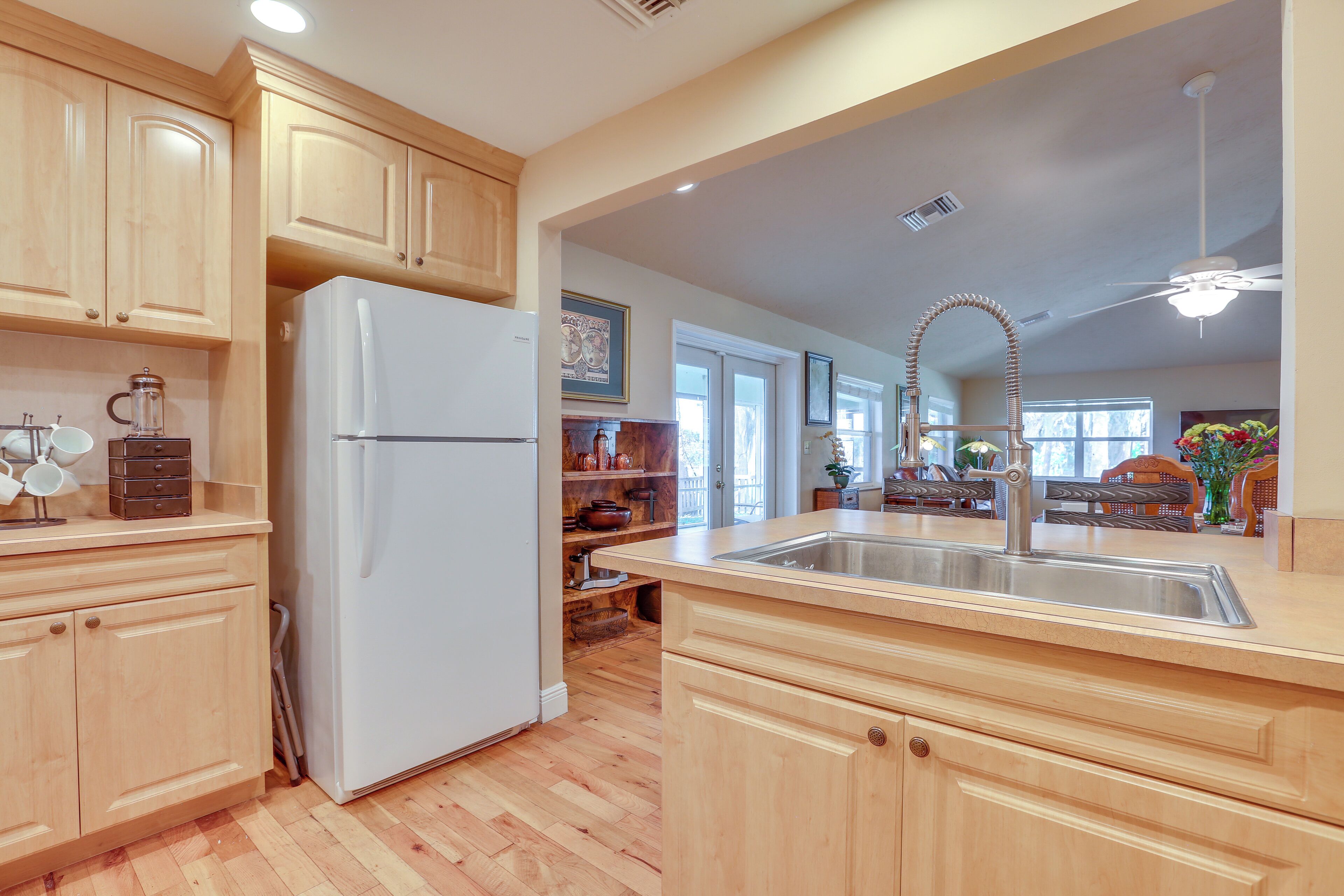 A kitchen with wooden cabinets, a white refrigerator, a stainless steel sink, and a ceiling fan.
