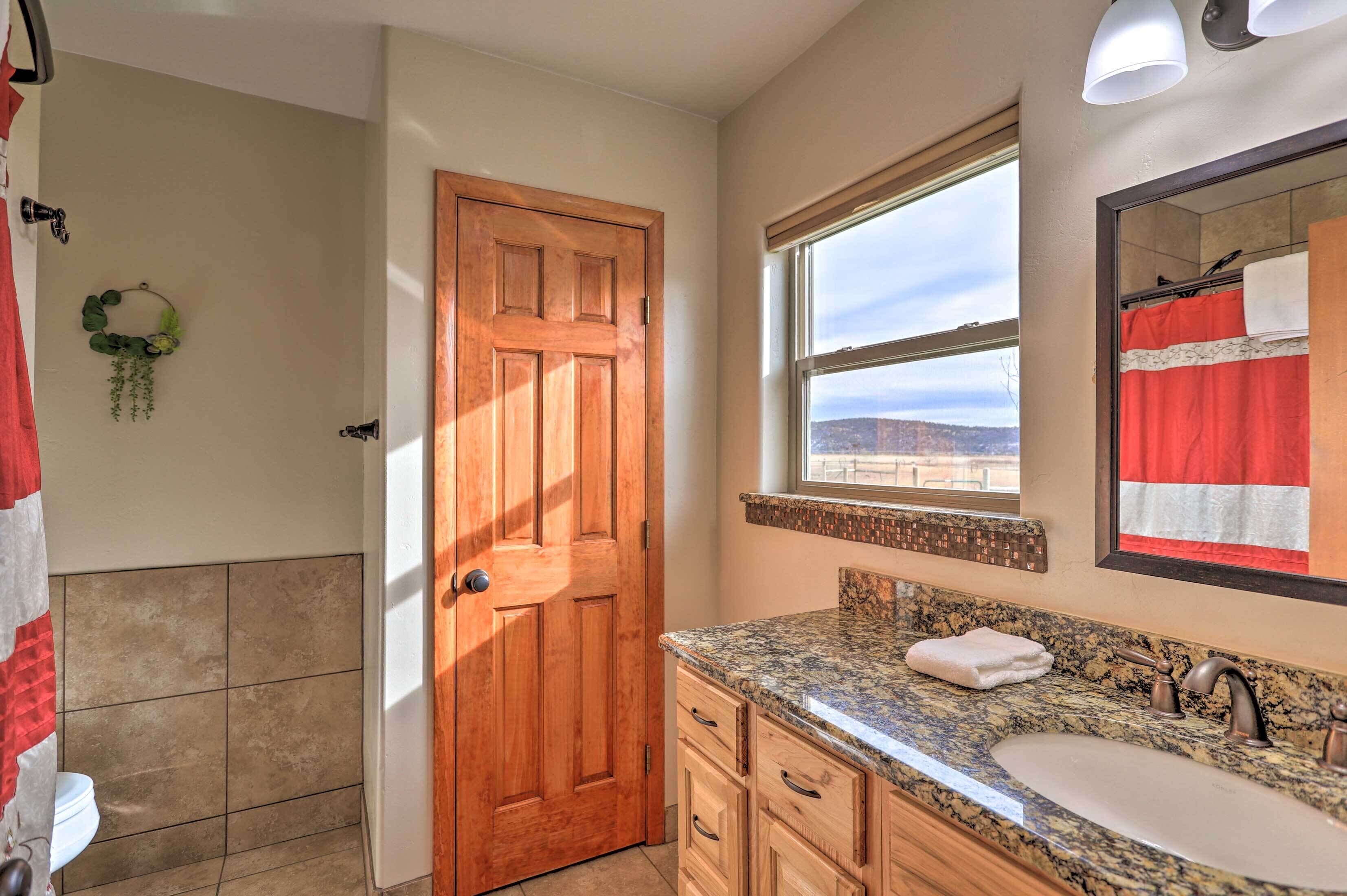 A bathroom with a wooden door, a large window, a granite countertop, and a sink.