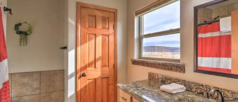 A bathroom with a wooden door, a large window, a granite countertop, and a sink.