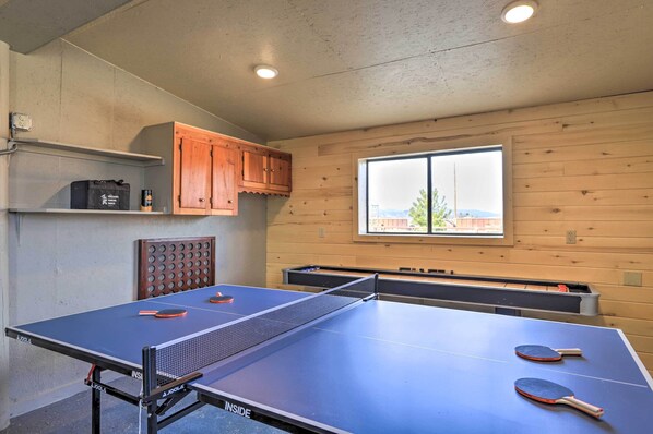 Een tafeltennistafel met twee batjes, een tafeltennisbal en een tas in een kamer met houten wanden en een raam.