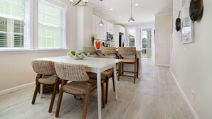 Une cuisine spacieuse avec des meubles blancs, une grande table à manger, des chaises en osier et des luminaires suspendus.