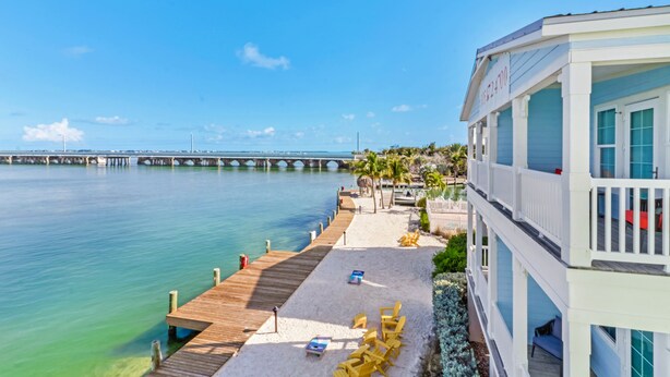 Un hôtel situé en bord de mer, doté d’une jetée en bois qui s’avance dans l’eau, d’un espace piscine avec des chaises longues et d’une vue sur un pont situé au loin.