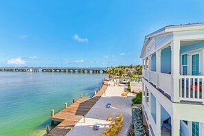 A beachfront hotel with a wooden pier extending into the water, a pool area with sun loungers, and a view of a bridge in the distance. - Little Torch Cottages (Summerland Key)