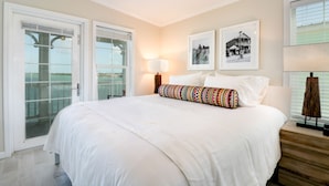 Une chambre d’hôtel avec un grand lit, un balcon avec des portes vitrées, un ventilateur de plafond et deux tableaux encadrés au mur.