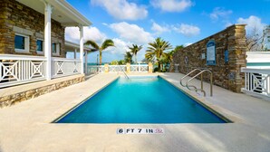 Une piscine dont la profondeur est indiquée à 6 pieds et 7 pouces, entourée de murs de pierre et de rampes blanches, sous un ciel bleu dégagé.