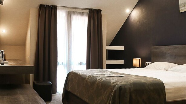 A modern hotel room with a bed, bedside table, and a desk with a chair. - Villa Hotel Tbilisi (თბილისი)