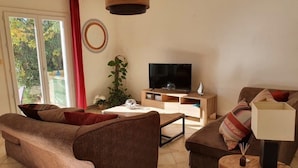 A living room with a sofa, coffee table, and TV stand. There is a plant and a window with curtains.