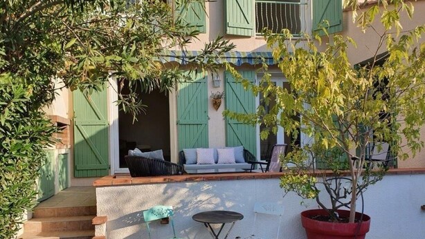 A patio with a small table and chairs, a potted plant, and a staircase leading to a building with green shutters.