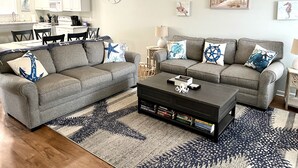 En stue med to grå sofaer, et sofabord og et bogreol. I baggrunden er der et spiseområde med et bord og stole.
