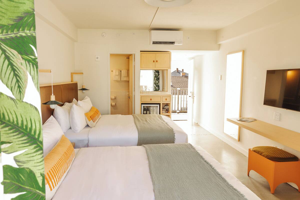 A hotel room with two beds, a TV, a small table, and a balcony with a view.