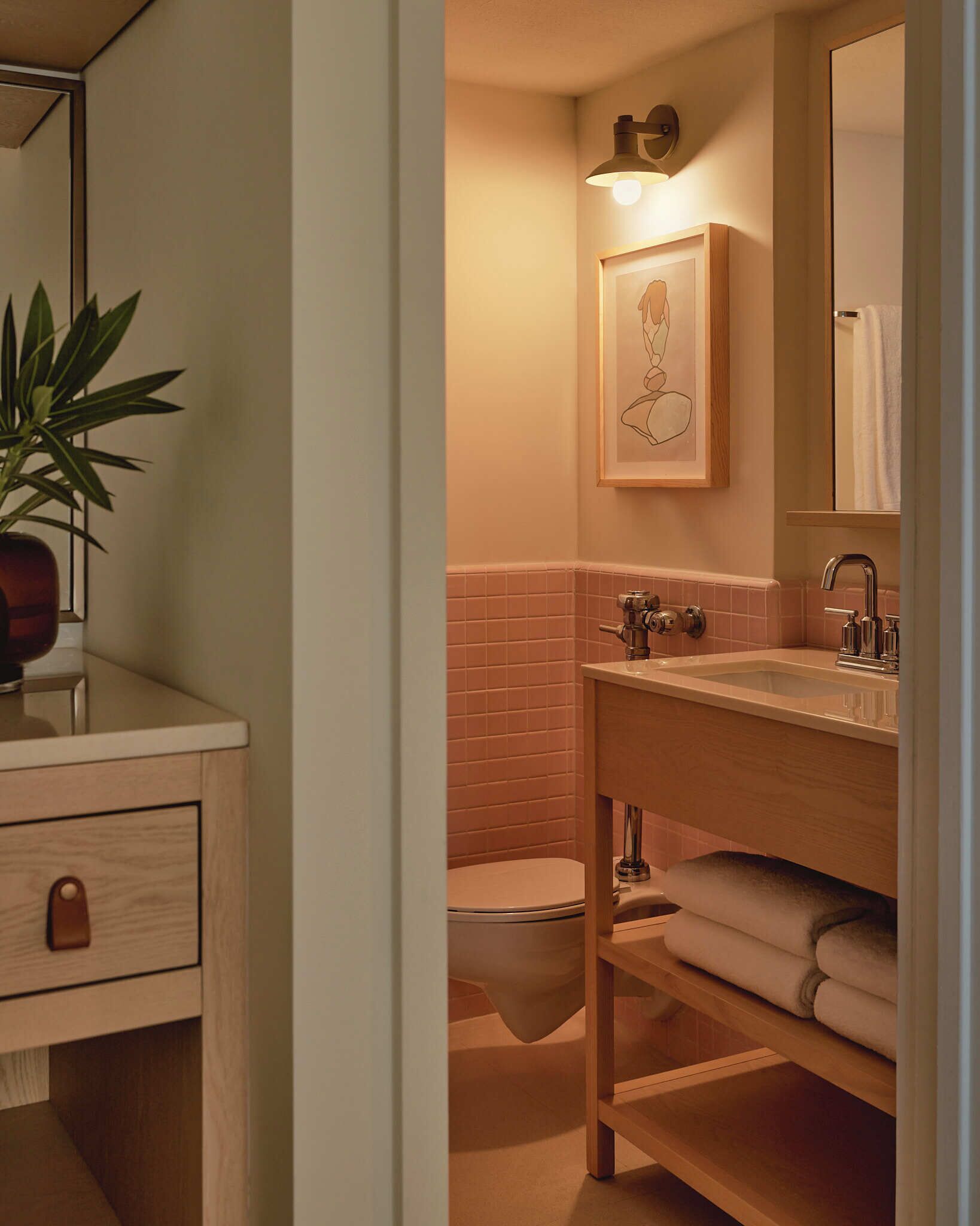 Un baño con tocador de madera, lavamanos, inodoro y una obra de arte enmarcada sobre el espejo.