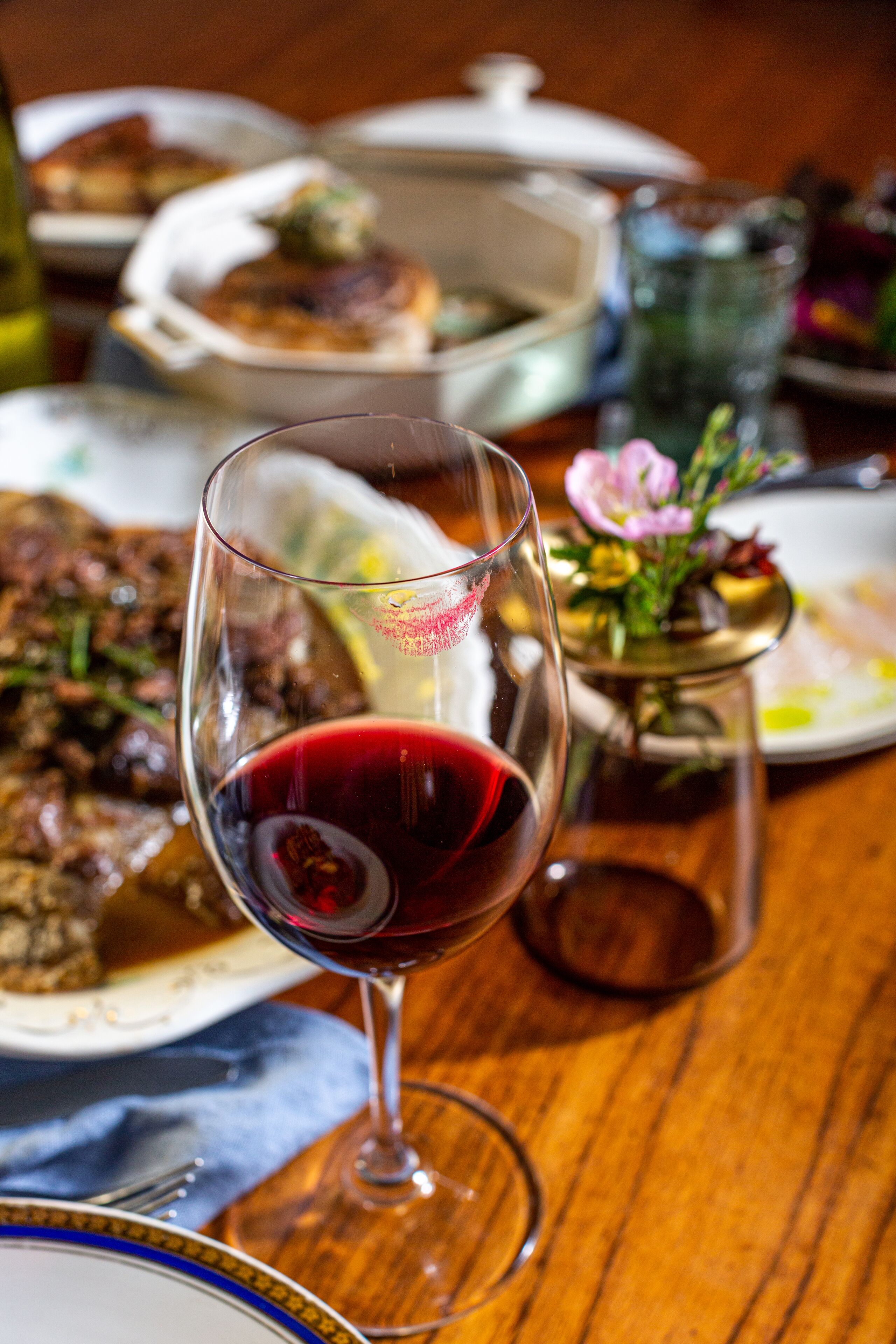 A dining table with a glass of red wine, a plate of food, and a small decorative vase.