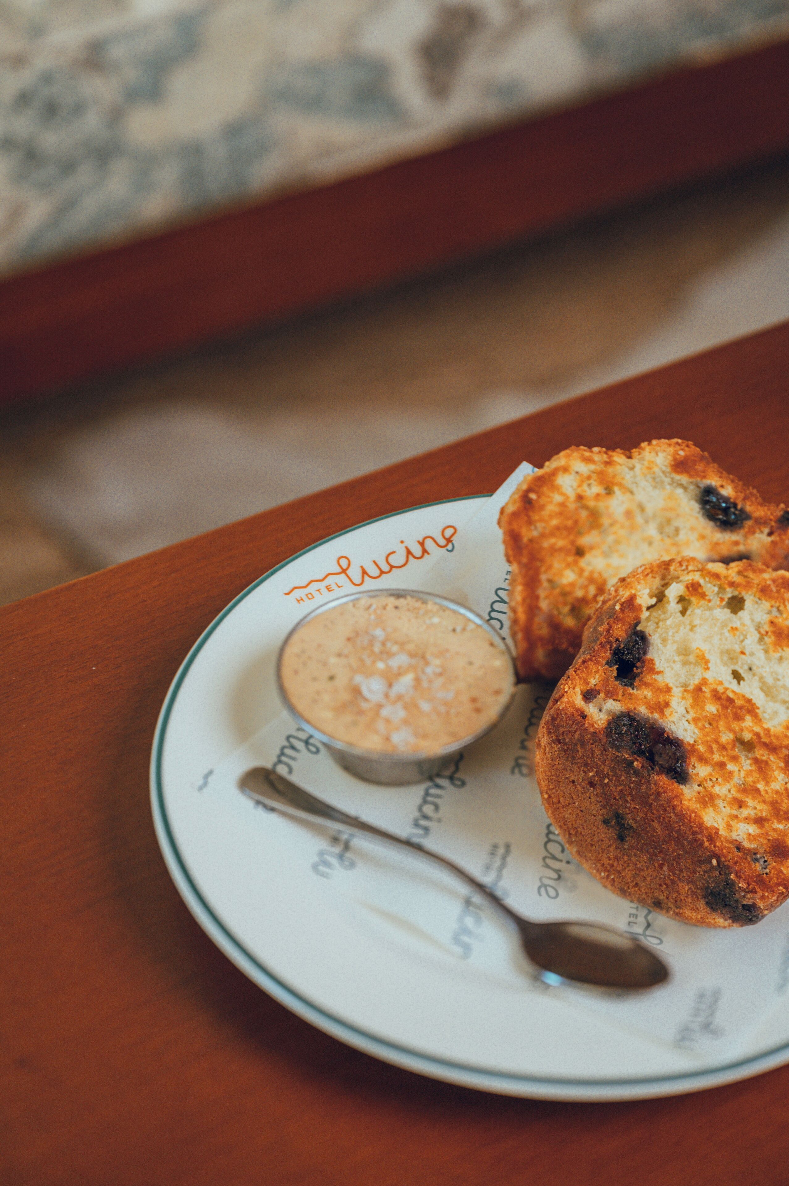 A plate with a muffin and a spoon, and a cup of coffee on a table.