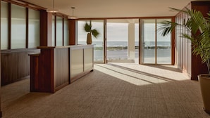 A spacious room with large windows, a wooden desk, and a potted plant. - Hotel Lucine (Galveston)