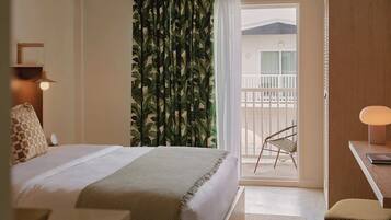 A hotel room with a bed, a desk, a chair, a balcony with a view, and a curtain with a leaf pattern.