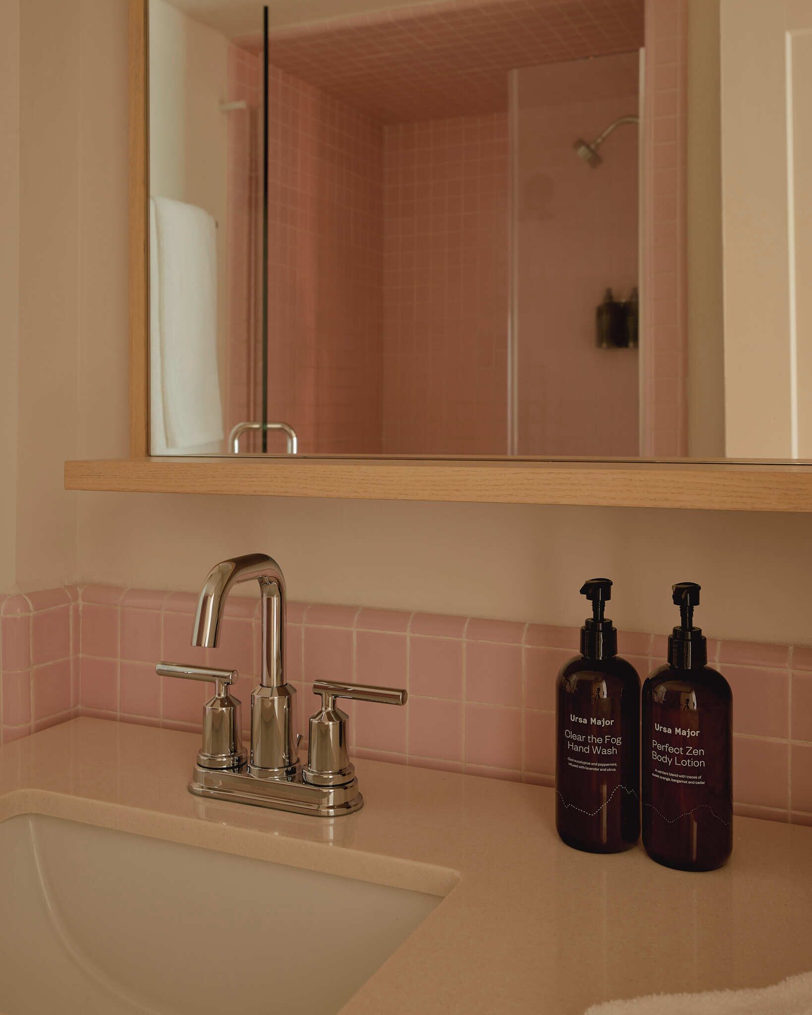 Un baño con lavamanos, dos botellas de jabón para manos y una ducha.
