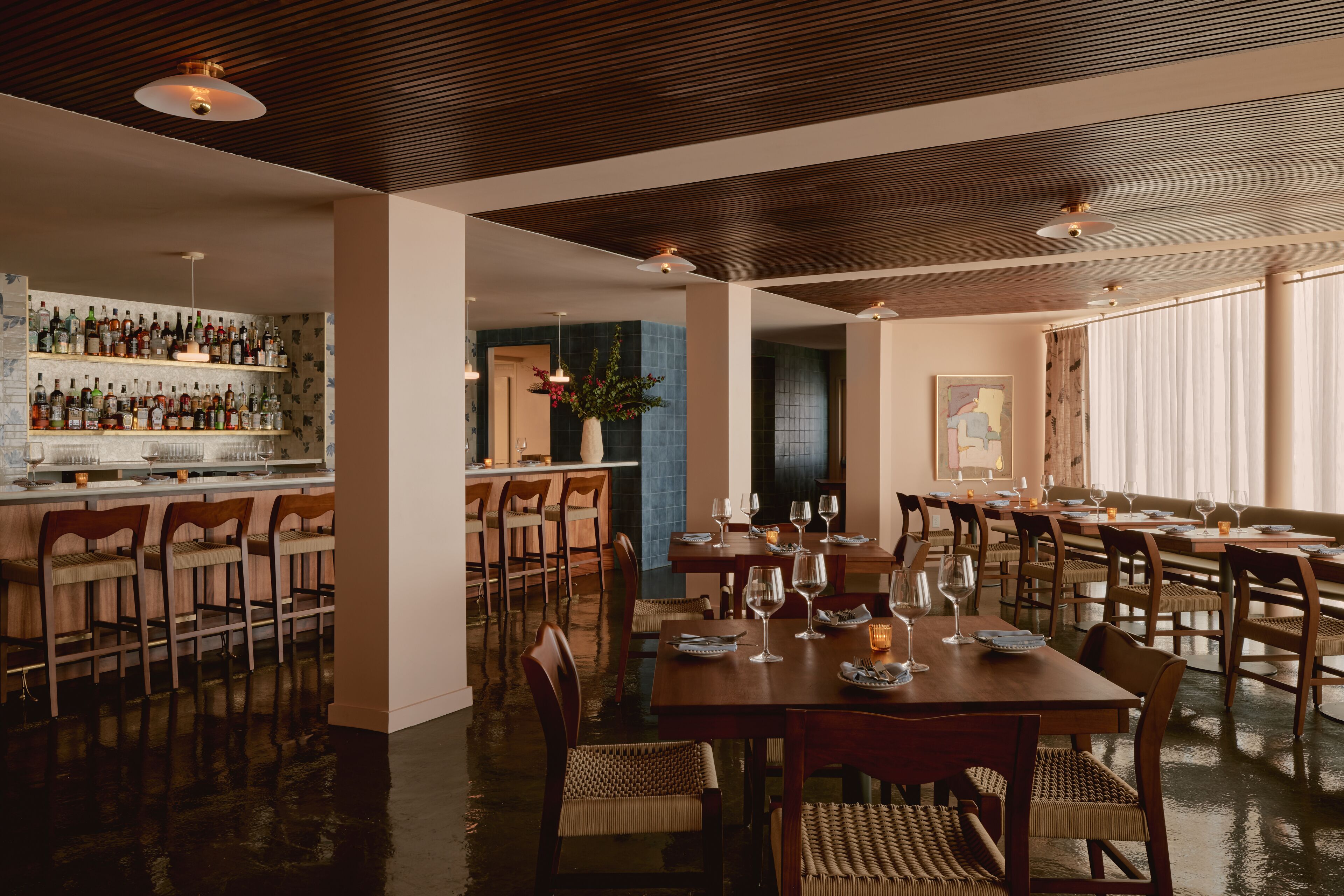 A restaurant with a bar area, wooden tables, and chairs.