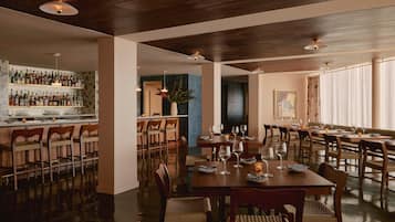A restaurant with a bar area, wooden tables, and chairs.